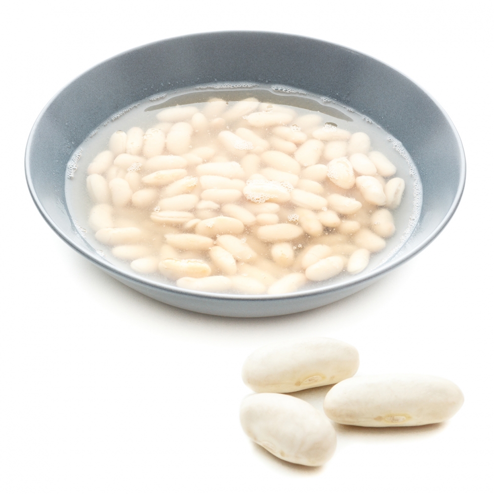 Imagen en la que se ve un plato de judías cocinados y tres judías crudas delante del plato