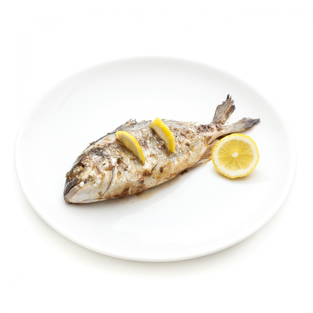 Imagen en la que se ve un pescado cocinado con limón sobre un plato