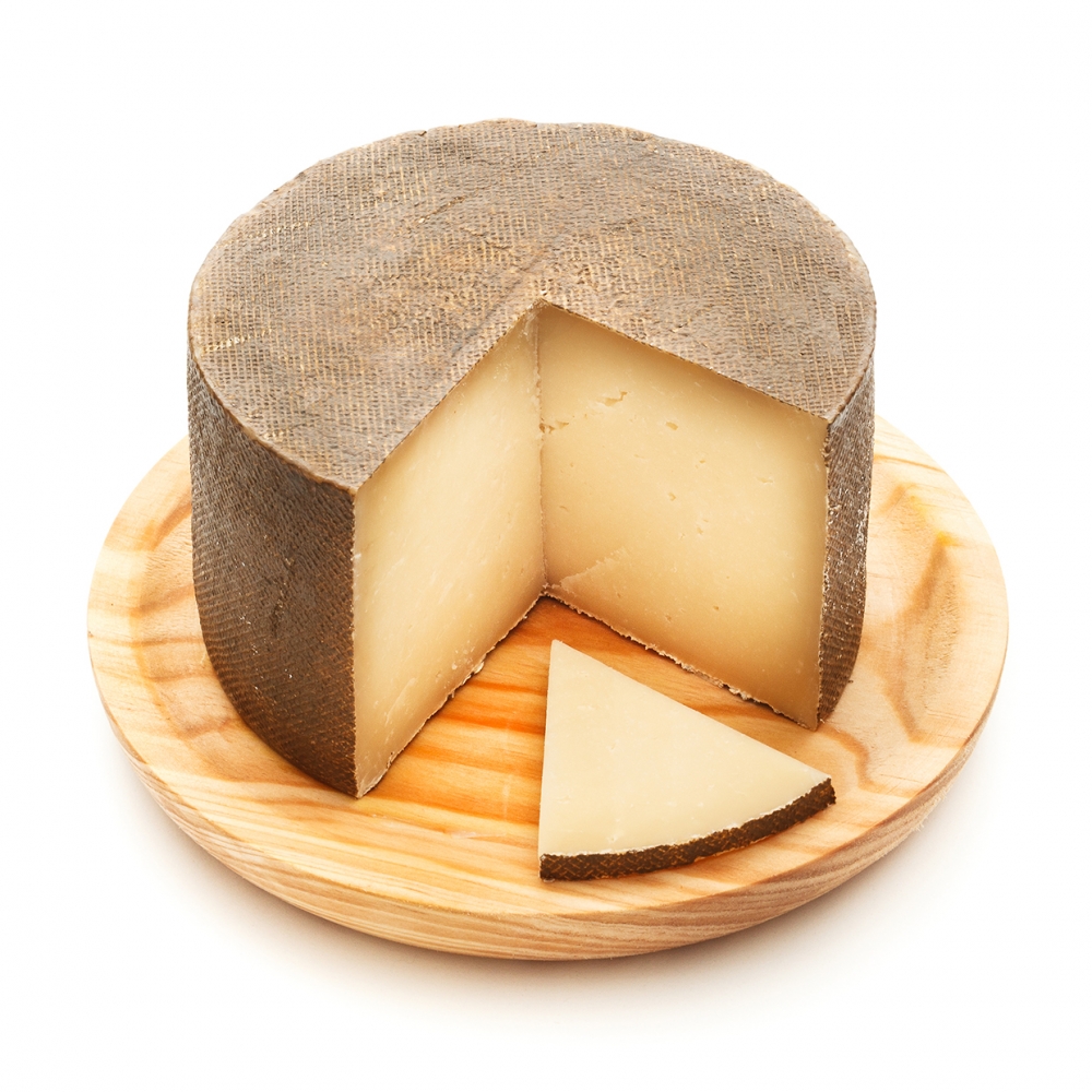 Imagen en la que se ve un queso al que le falta un cuarto. Delante de él hay una loncha de queso.
