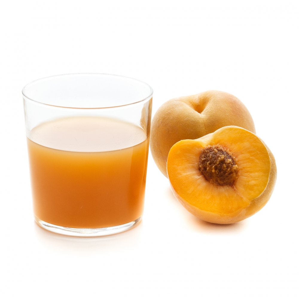 Imagen en la que se ve un vaso con zumo de melocotón y, a su lado, un melocotón entero y otro partido por la mitad delante.