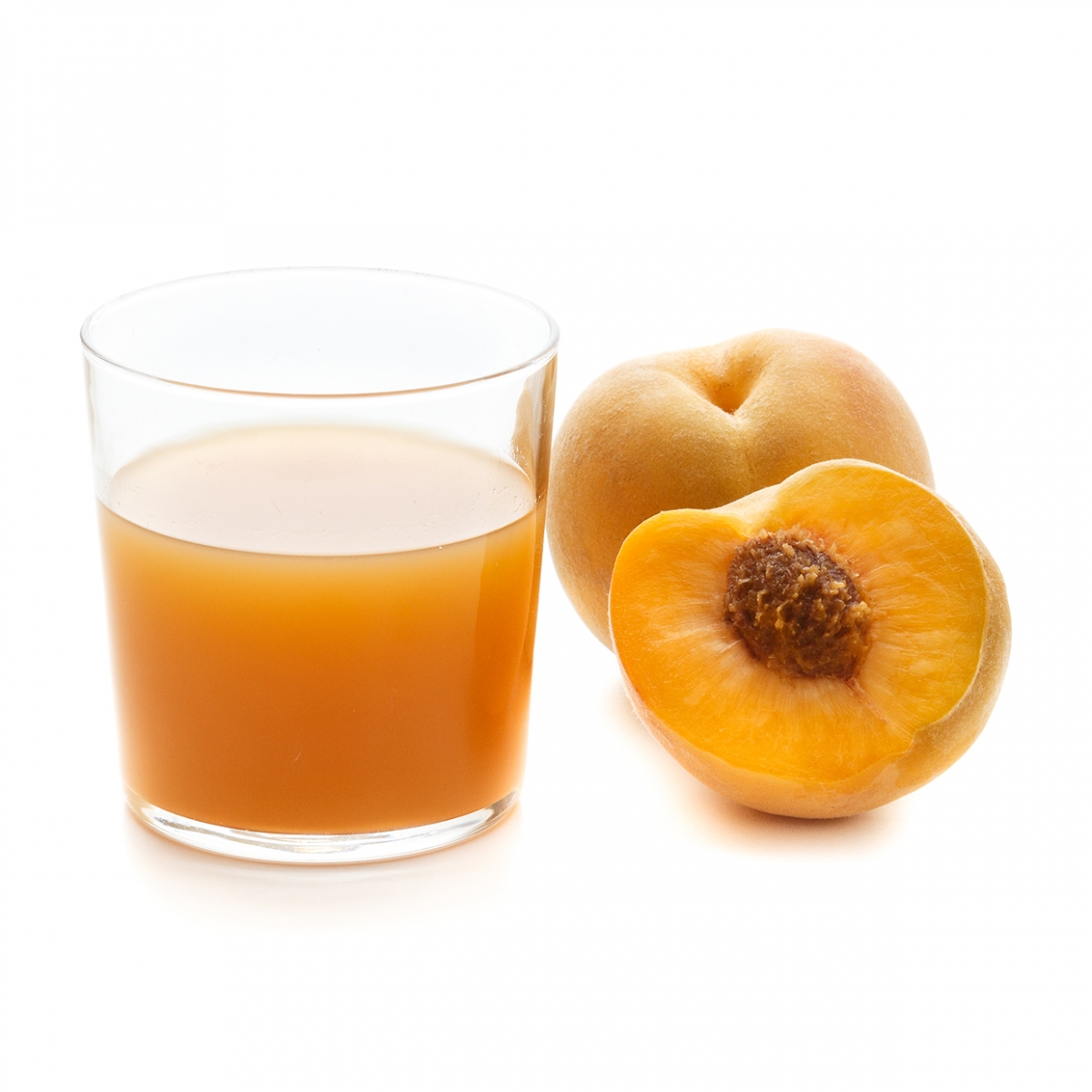 Imagen en la que se ve un vaso con zumo de melocotón y, a su lado, un melocotón entero y otro partido por la mitad delante.