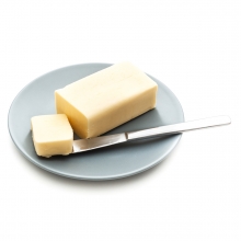 Imagen en la que se ve un bloque de mantequilla sobre un plato y con un trozo cortado encima de un cuchillo