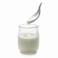 Imagen en la que se ve un recipiente de cristal con yogur en su interior y una cucharilla saliendo del mismo