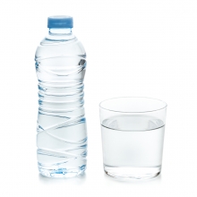 Imagen en la que se ve una botella de plástico llena de agua con un vaso lleno de agua a su lado