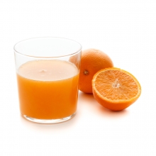 Imagen en la que se ve un vaso con zumo de naranja y, a su lado, una naranja entera y otra partida por la mitad delante.